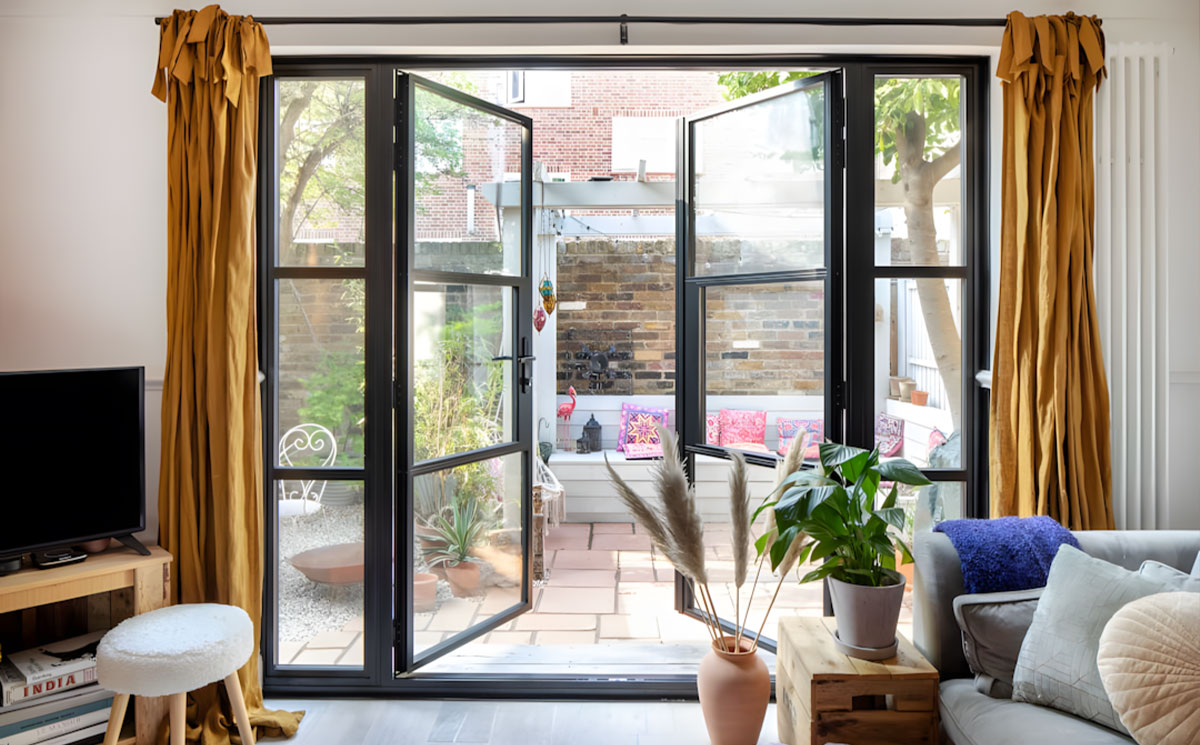 Modern minimalist black narrow frame glass doors opening to outdoor courtyard patio