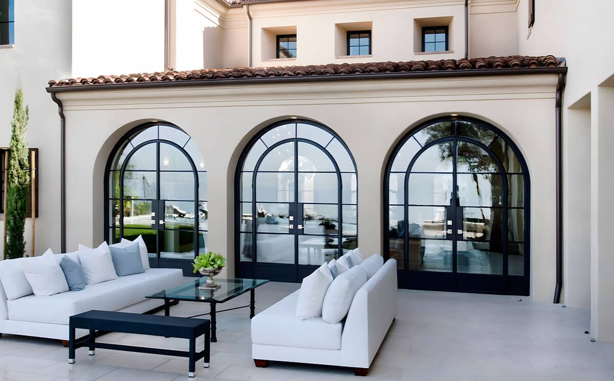 French style arched ultra slim frame black metal glass French swing doors set in a triple arch configuration connecting villa living room to outdoor patio terrace
