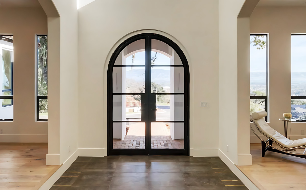 French style arched slim frame black metal double glass swing door installed in an entry foyer hallway transition with oak hardwood flooring