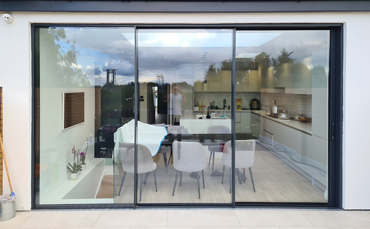 Aluminum sliding glass door connecting contemporary indoor kitchen and dining area to outdoor patio